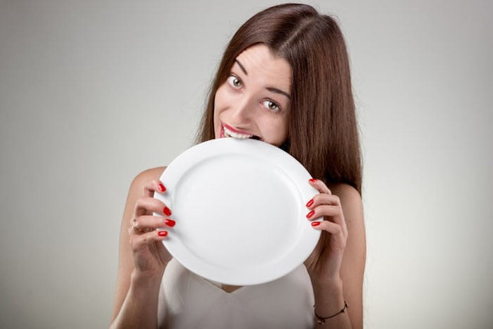 Thiếu nữ đói cầm chiếc đĩa trắng và cắn vào đó, thể hiện sự đói khát và thèm ăn.